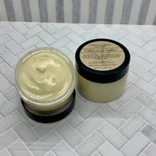 Load image into Gallery viewer, Two jars of tallow body butter on a textured surface with a striped background