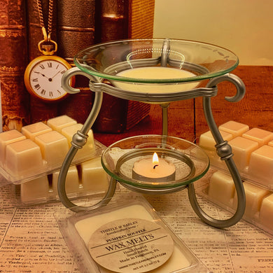 Wax melt burner with wax melts and a candle on a surface with books and a clock in the background.